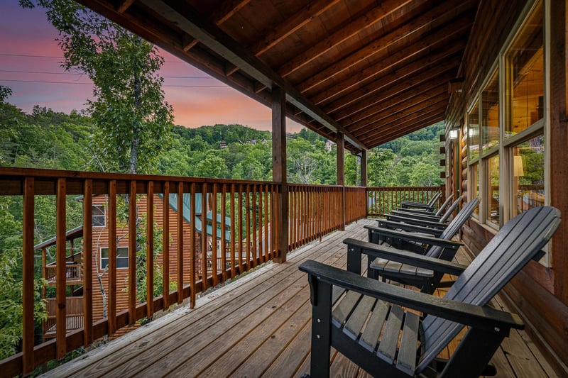 This spacious deck overlooks lush wooded hills framed by a stunning sunset sky, perfect for relaxing in comfortable Adirondack chairs and soaking in the tranquil mountain views.