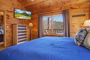 Unwind in your cozy cabin bedroom with rustic wood walls, mountain views from your window, and modern TV for relaxing evenings.