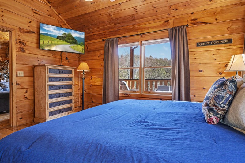 Unwind in your cozy cabin bedroom with rustic wood walls, mountain views from your window, and modern TV for relaxing evenings.