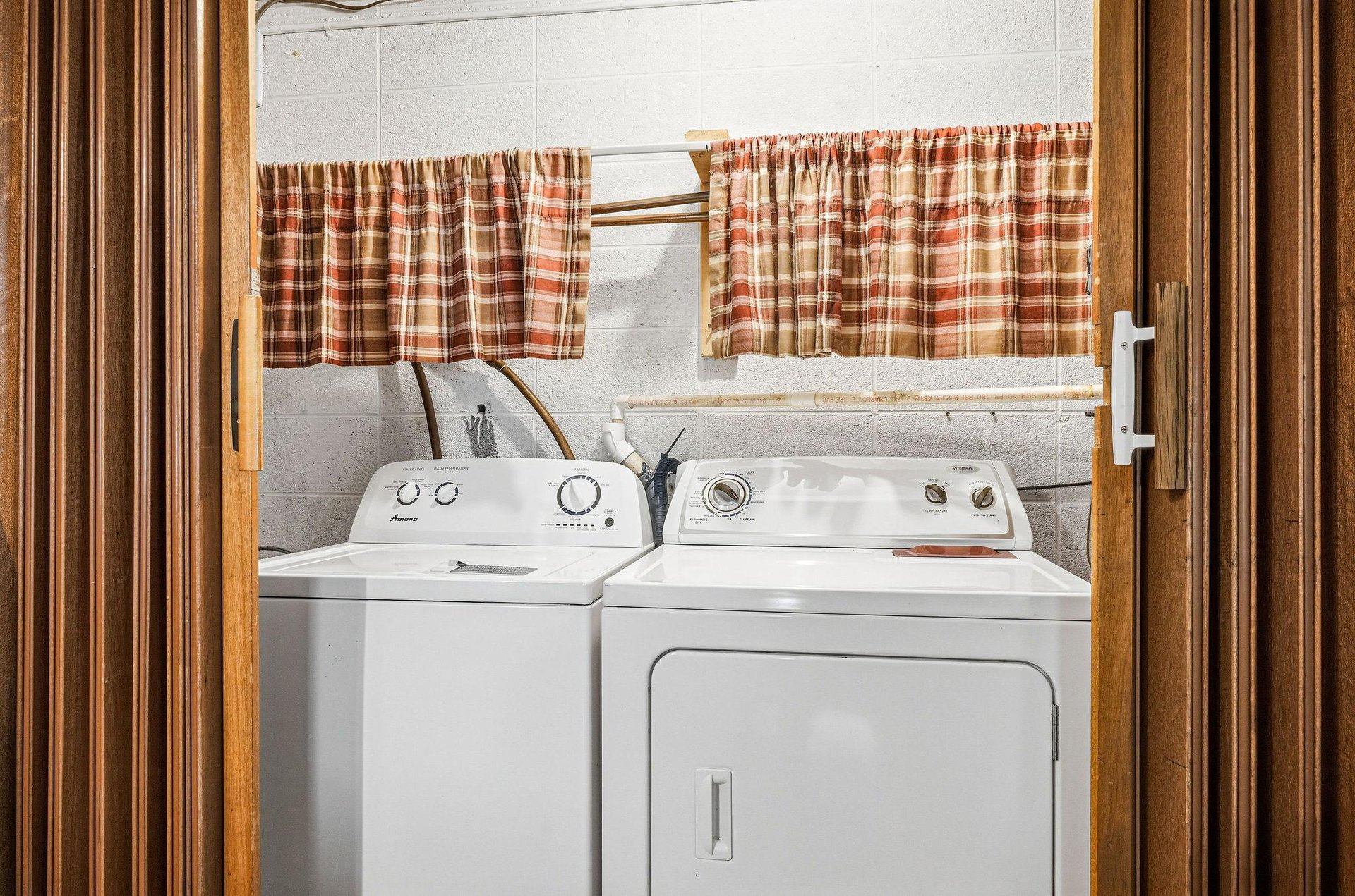 Your laundry stays fresh and convenient with a full washer and dryer set, complete with cheerful plaid curtains brightening this practical space.