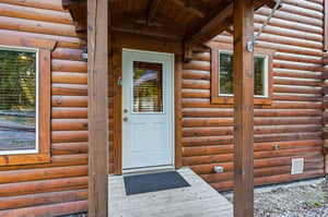 The entrance to this charming log cabin features a welcoming covered porch and classic timber construction that sets the tone for a peaceful mountain retreat.