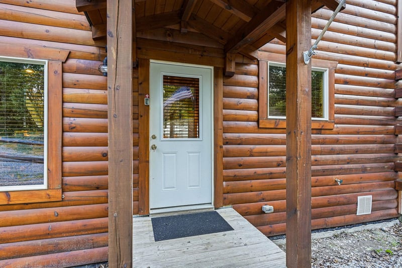 The entrance to this charming log cabin features a welcoming covered porch and classic timber construction that sets the tone for a peaceful mountain retreat.