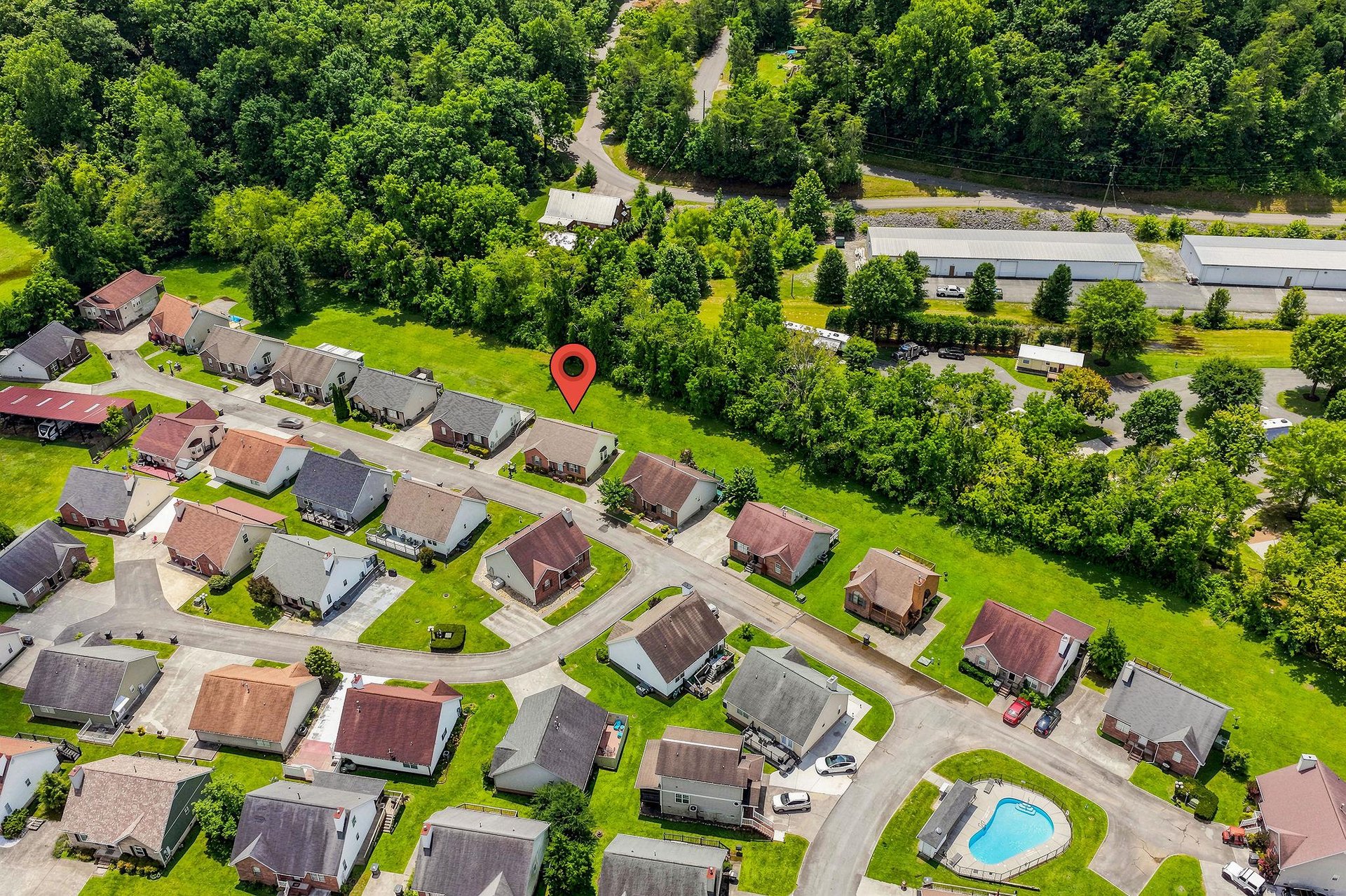 Aerial view of a peaceful residential neighborhood surrounded by lush greenery, with treelined streets and a nearby pool area for community leisure.