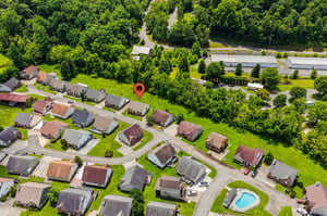 Aerial view of a peaceful residential neighborhood surrounded by lush greenery, with treelined streets and a nearby pool area for community leisure.