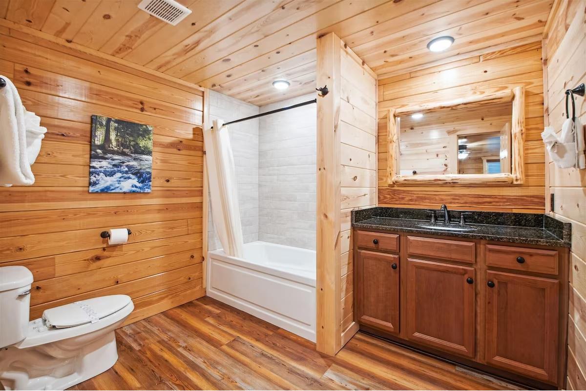 Unwind in your rustic cabin bathroom with warm wood walls, granite vanity, and a relaxing tubshower combo surrounded by cozy mountain lodge charm.