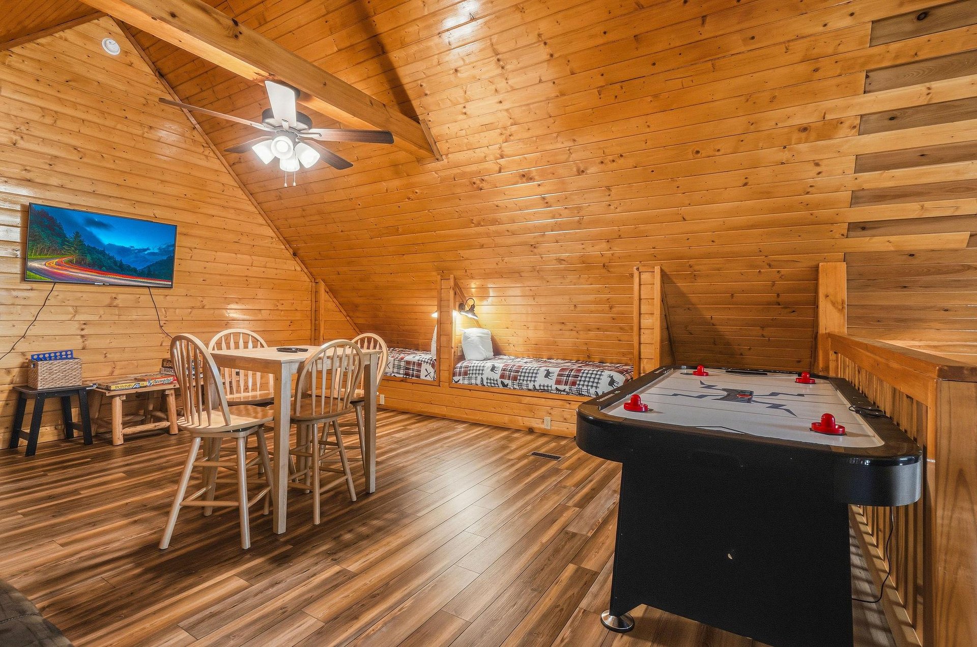 Your cozy loft game room invites friendly competition with air hockey and a dining table, all beneath warm wood beams and vaulted ceilings that make every moment feel like a mountain getaway.