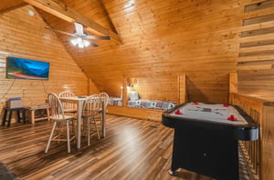 Your cozy loft game room invites friendly competition with air hockey and a dining table, all beneath warm wood beams and vaulted ceilings that make every moment feel like a mountain getaway.