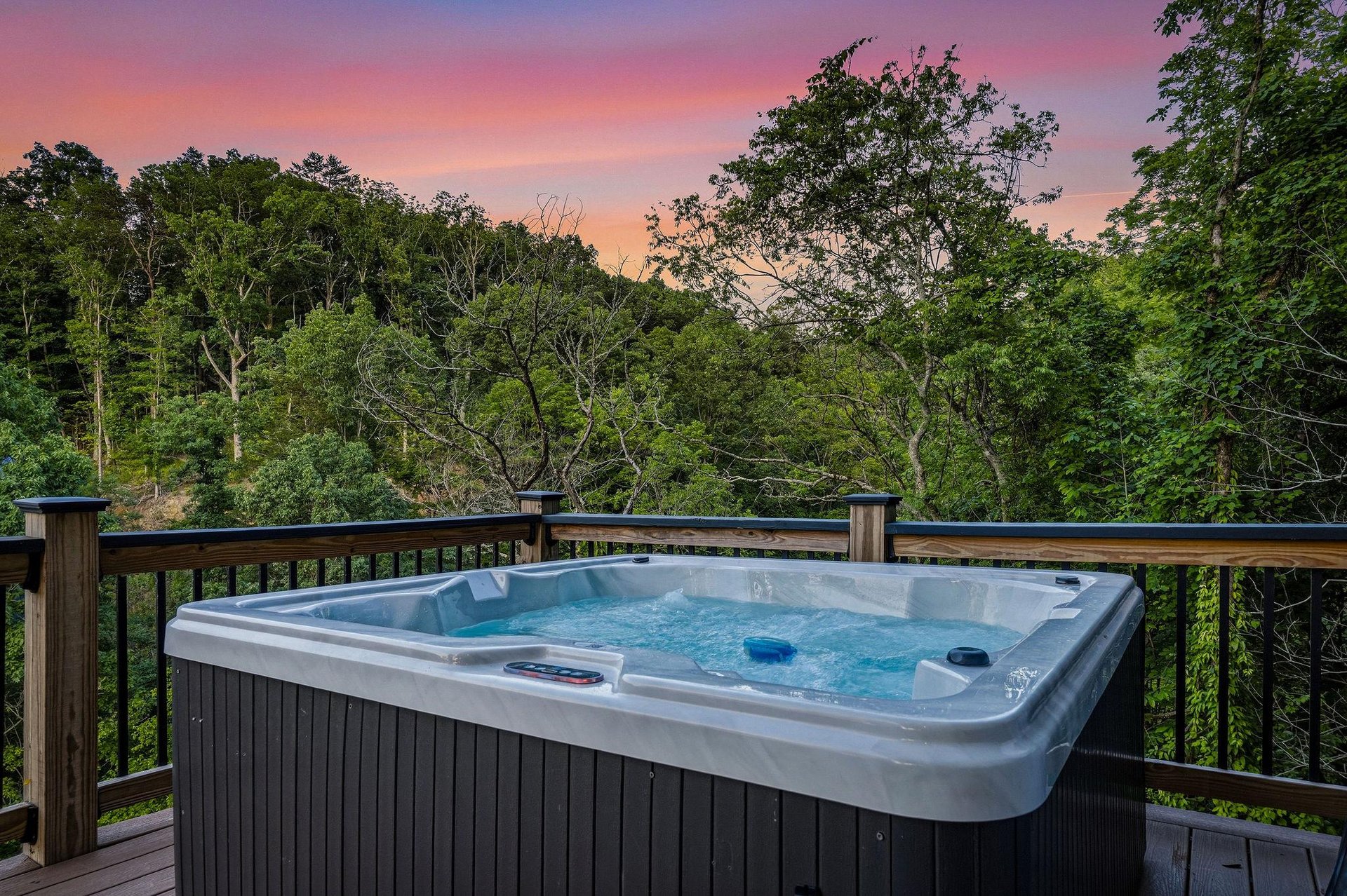 A private hot tub on the deck showcases stunning natural surroundings beneath a painted sunset sky—a perfect spot for you to unwind and soak in the beauty.