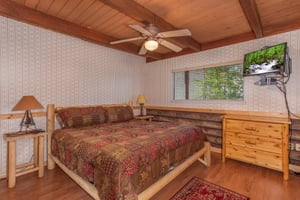 Bedroom with a kingsized log bed, dresser, and television at Bushwood Lodge, a 3bedroom cabin rental located in Gatlinburg