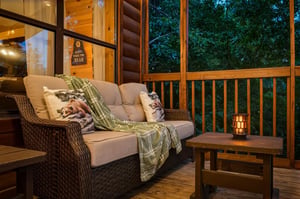 Sink into this cozy screened porch with plush seating, warm lantern light, and peaceful wooded surroundings—perfect for your evening unwind.