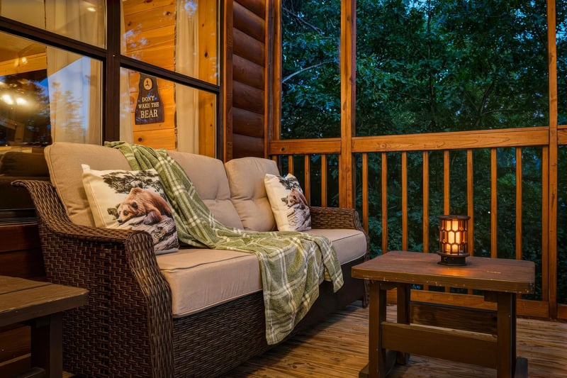 Sink into this cozy screened porch with plush seating, warm lantern light, and peaceful wooded surroundings—perfect for your evening unwind.