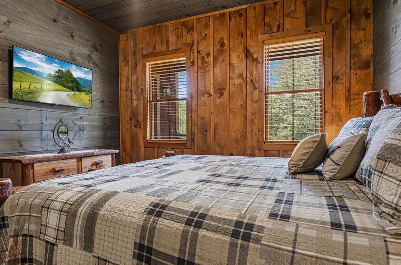 Unwind in your cozy cabin bedroom with rustic wood walls, plush plaid bedding, and soft natural light streaming through the windows. Your perfect mountain retreat awaits.