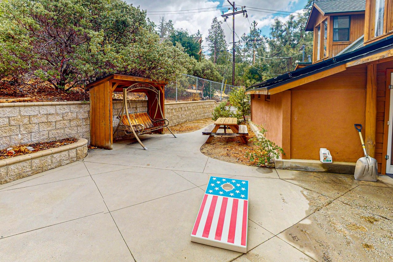 The fenced backyard features a picnic table and a covered porch swing, plus a utility room visible here housing the washerdryer, an extra refrigerator, hot tub towels, and games for the kids — with the cornhole set stored inside when not in use.