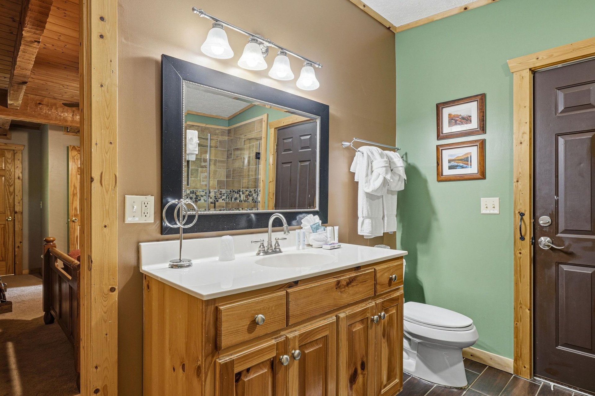 Your private bathroom features a spacious vanity with warm wood cabinetry and fresh white towels waiting for you. The combination of natural wood and calming green walls creates a serene and welcoming