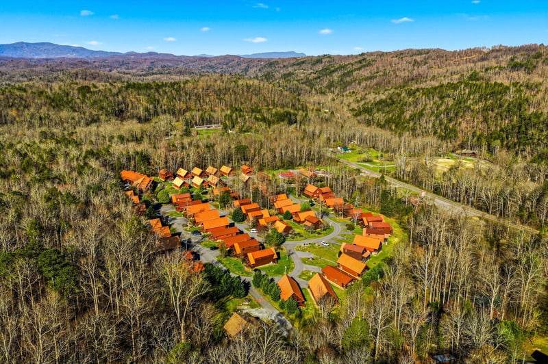 Aerial view of a rustic cabin resort nestled in pristine wilderness, surrounded by rolling mountains and endless forest views.