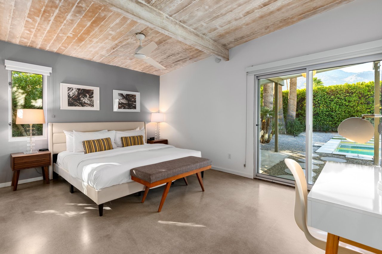 Wake to sun streaming through floortoceiling windows in your stylish bedroom, where rustic wood beams blend with modern comfort and pool views.
