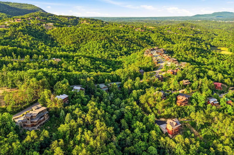 Aerial view of vacation cabins nestled among rolling forested mountains, showcasing the propertys secluded natural setting in a lush, expansive landscape.
