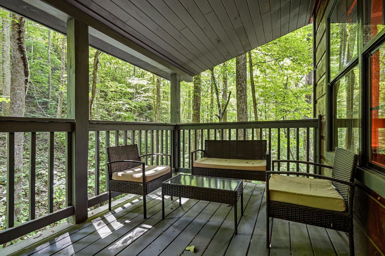 Step onto your private covered porch and sink into comfortable wicker seating surrounded by peaceful forest views—your perfect spot to sip morning coffee or unwind after a day of adventure.