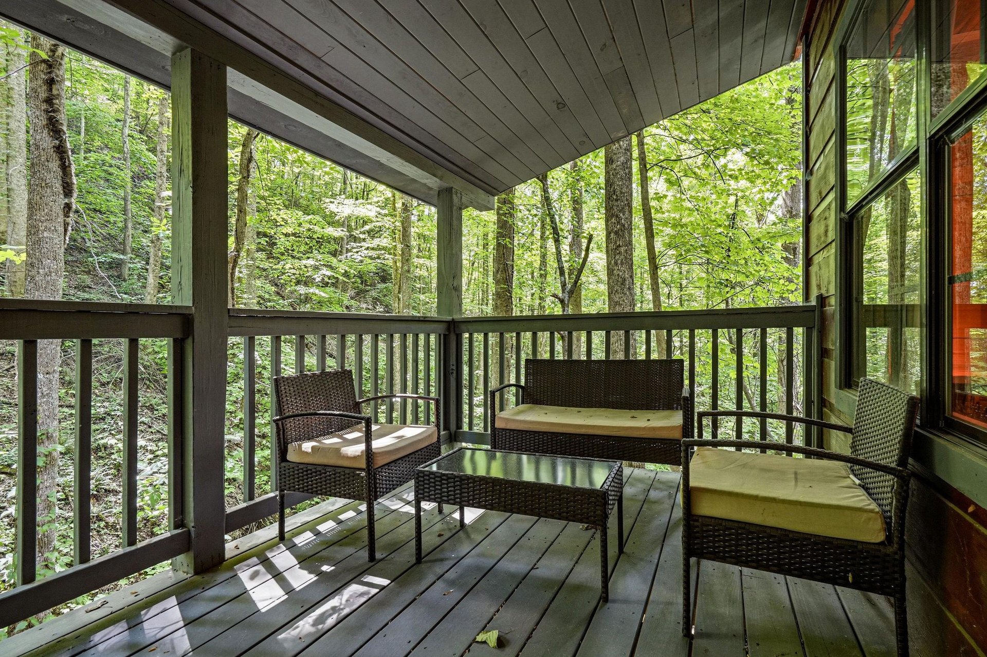 Step onto your private covered porch and sink into comfortable wicker seating surrounded by peaceful forest views—your perfect spot to sip morning coffee or unwind after a day of adventure.