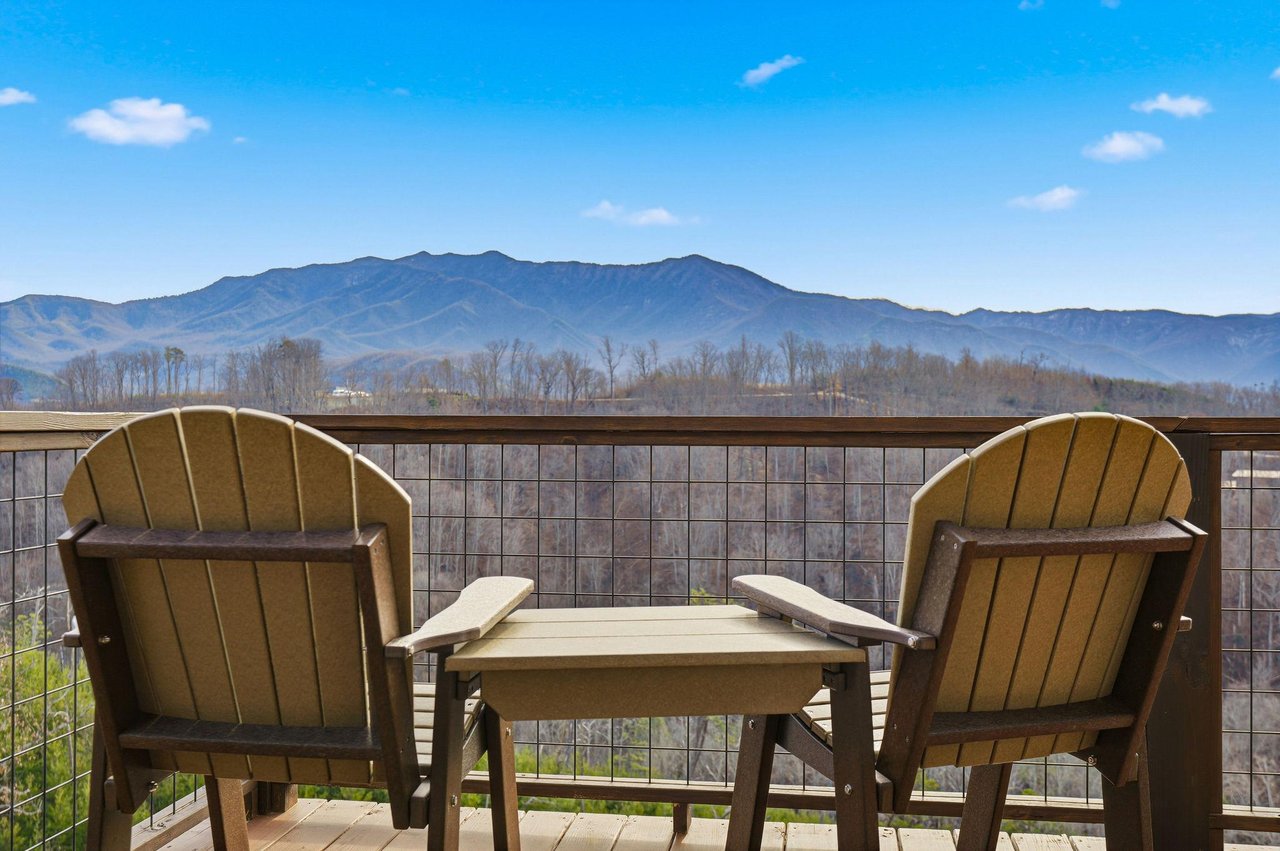 Private balcony seating overlooks stunning mountain ranges under brilliant blue skies.