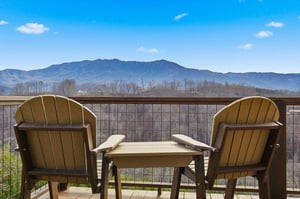 Private balcony seating overlooks stunning mountain ranges under brilliant blue skies.