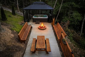 Private outdoor retreat featuring hot tub, fire pit, and wooden seating nestled in a peaceful forest setting—perfect for your memorable evenings under the stars.