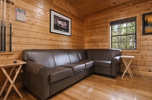 Relax in your cozy cabin living room with rustic wood walls, comfortable leather sectional, and scenic views through large windows.