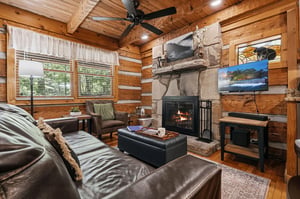 Picture yourself unwinding in this cozy cabin living room with warm wood walls, a crackling stone fireplace, and plush leather seating that invites you to relax after a day of adventure.