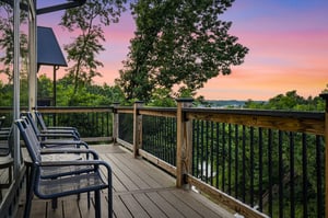 Elevated deck overlooking lush forested landscape with vibrant sunset sky, featuring outdoor seating area perfect for evening relaxation.
