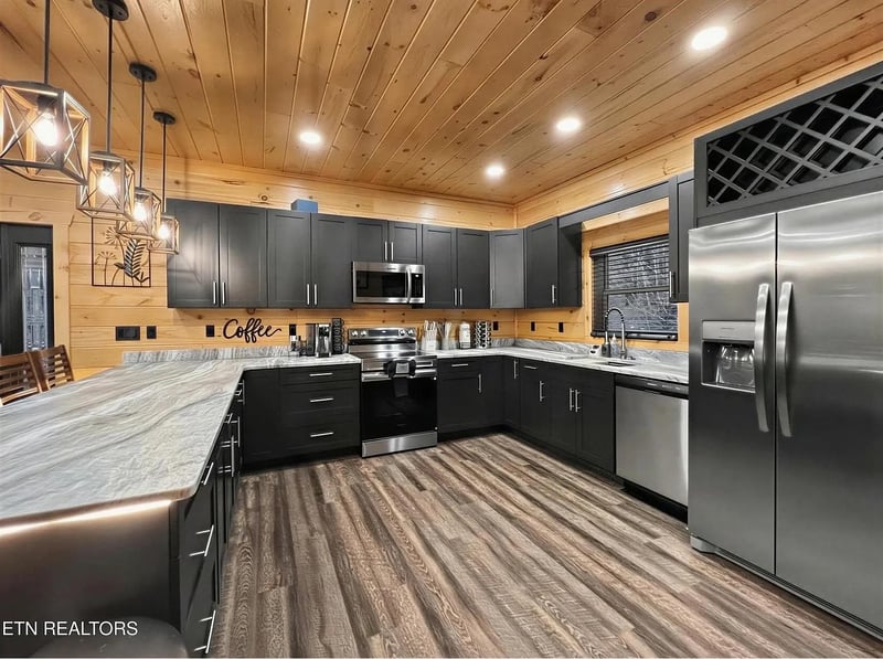 Cook delicious meals in this modern kitchen featuring stainless steel appliances, granite counters, and warm wood ceilings that create a cozy cabin atmosphere.