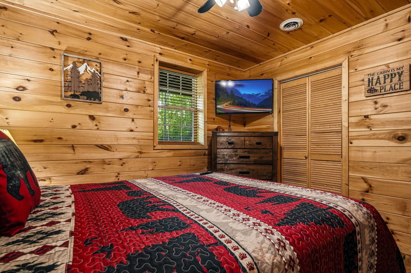 Drift off surrounded by warm knotty pine and rustic charm—your cozy cabin bedroom awaits with plush bedding, a mounted TV, and thoughtful touches that invite you to unwind completely.