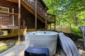 The property features an outdoor hot tub surrounded by lush greenery, offering a private retreat beneath mature trees and wooded seclusion.