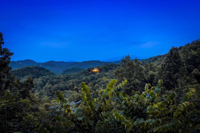The property sits nestled in the surrounding mountainous terrain, with forested hillsides and a distant structure visible against the evening sky.