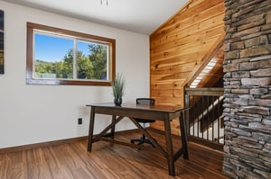 Warm wood paneling and stone accents create a cozy, rustic workspace overlooking lush greenery. Your perfect retreat for work or quiet moments.