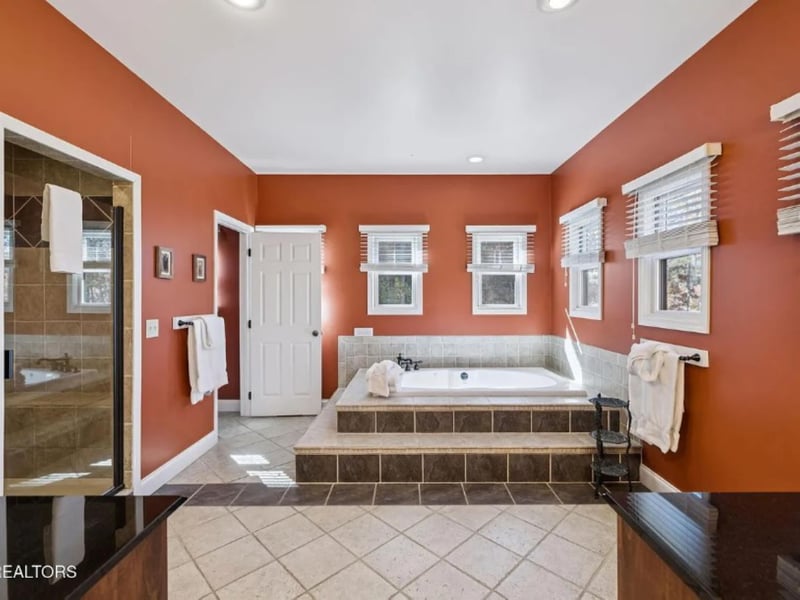 Your private retreat features a luxurious soaking tub set in tile surround, with warm terracotta walls and abundant natural light pouring in through crisp whitetrimmed windows.