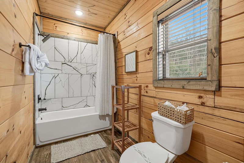Unwind in your rustic bathroom featuring marblelook tile shower, warm wood walls, and charming ladder towel rack.