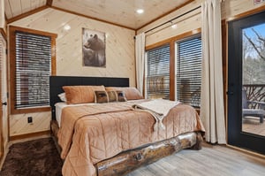 Drift off in your rustic cabin bedroom with warm earth tones, cozy bearthemed decor, and private balcony access for peaceful mornings.