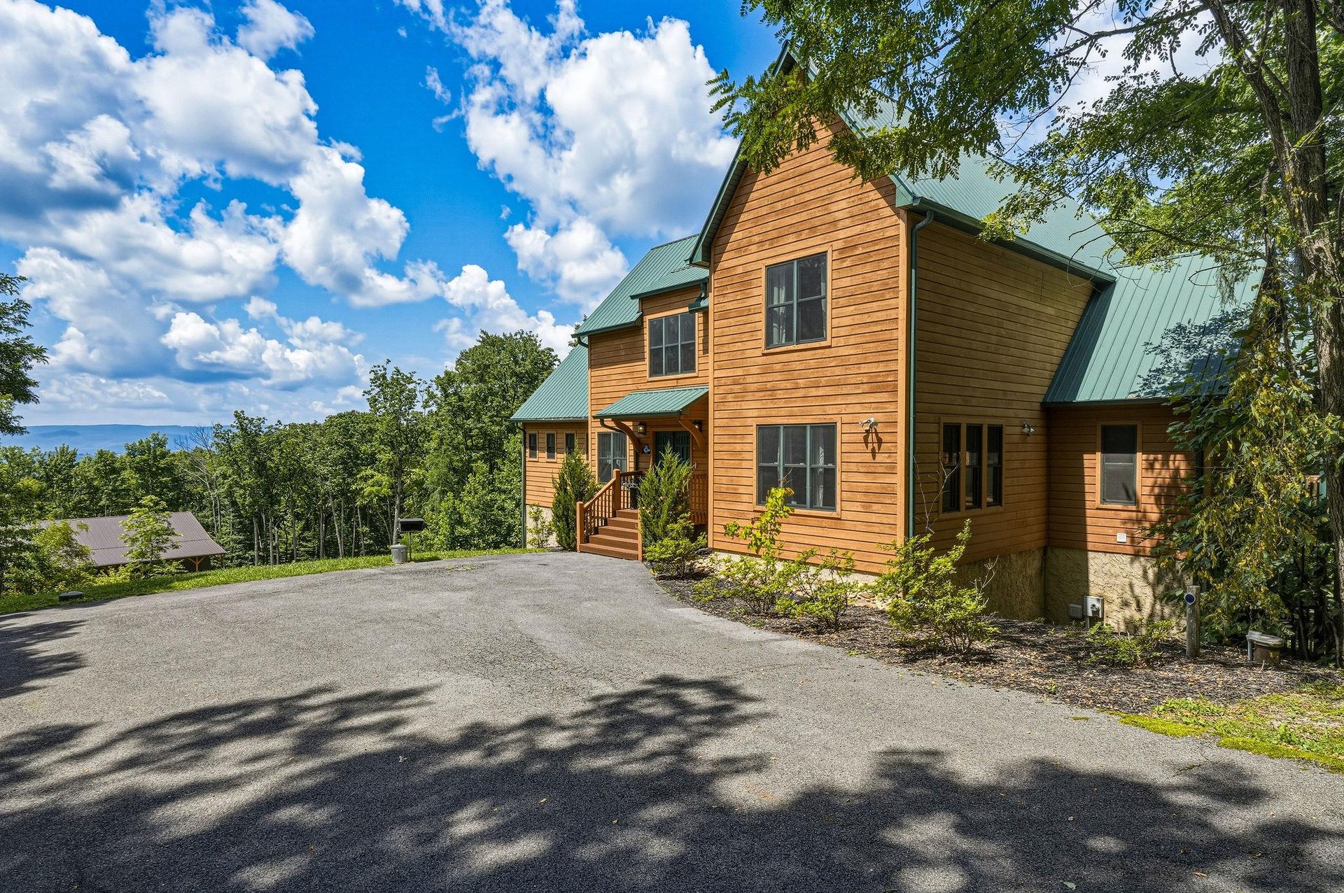 Charming mountain retreat with natural wood siding, nestled among mature trees with scenic views. The property features convenient parking and a welcoming covered entrance.