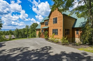 Charming mountain retreat with natural wood siding, nestled among mature trees with scenic views. The property features convenient parking and a welcoming covered entrance.