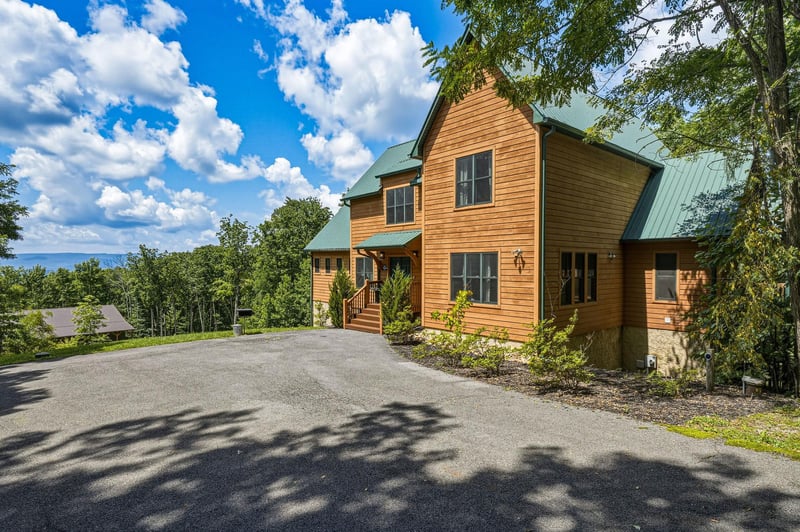 Charming mountain retreat with natural wood siding, nestled among mature trees with scenic views. The property features convenient parking and a welcoming covered entrance.