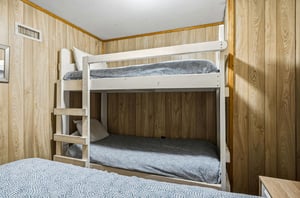 Cozy bunk bed setup with fresh linens awaits your family in this warm, woodpaneled bedroom.