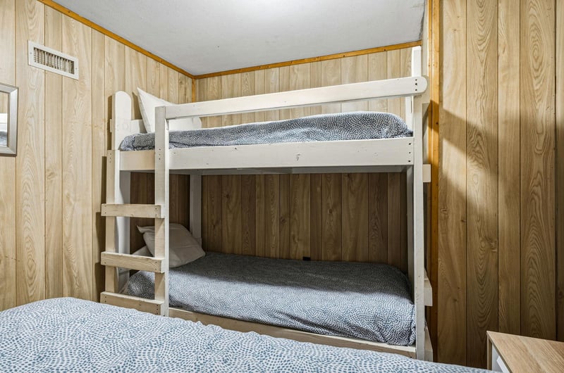 Cozy bunk bed setup with fresh linens awaits your family in this warm, woodpaneled bedroom.