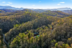 Aerial view of mountain retreat nestled among rolling forested hills with distant Blue Ridge peaks visible on the horizon.