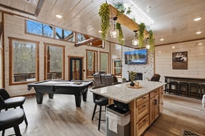 Unwind in your spacious game room with pool table, cozy fireplace, and stunning forest views through floortoceiling windows.