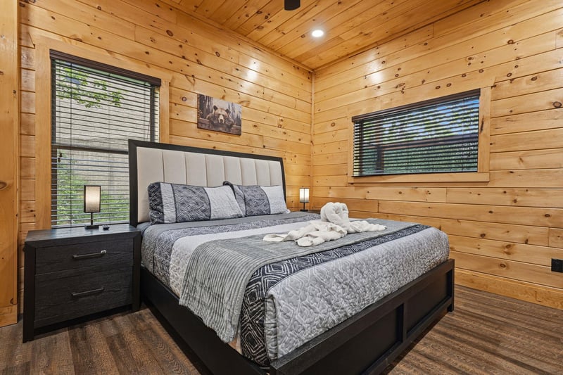 Unwind in this cozy log cabin bedroom where warm wood walls embrace your modern king bed, complete with plush towels and peaceful forest views.