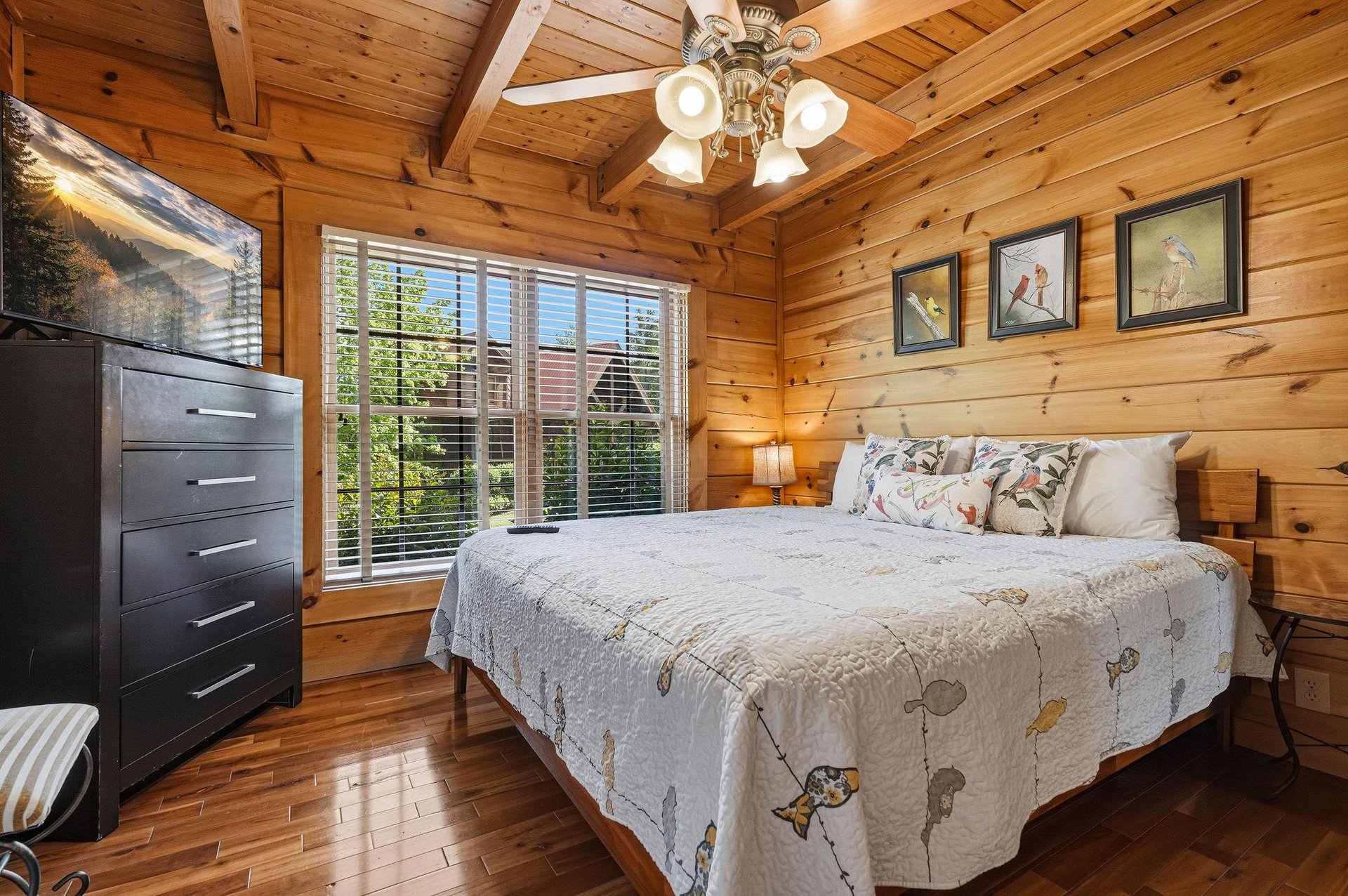 Unwind in your rustic cabin bedroom featuring warm wood walls, soft linens, and peaceful garden views through large windows.