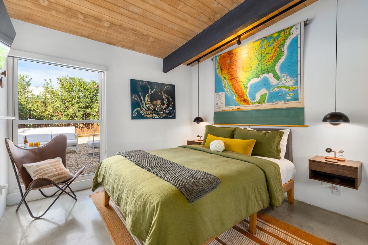 Unwind in your stylish bedroom featuring warm wood beams, vibrant green linens, and peaceful garden views through large windows.