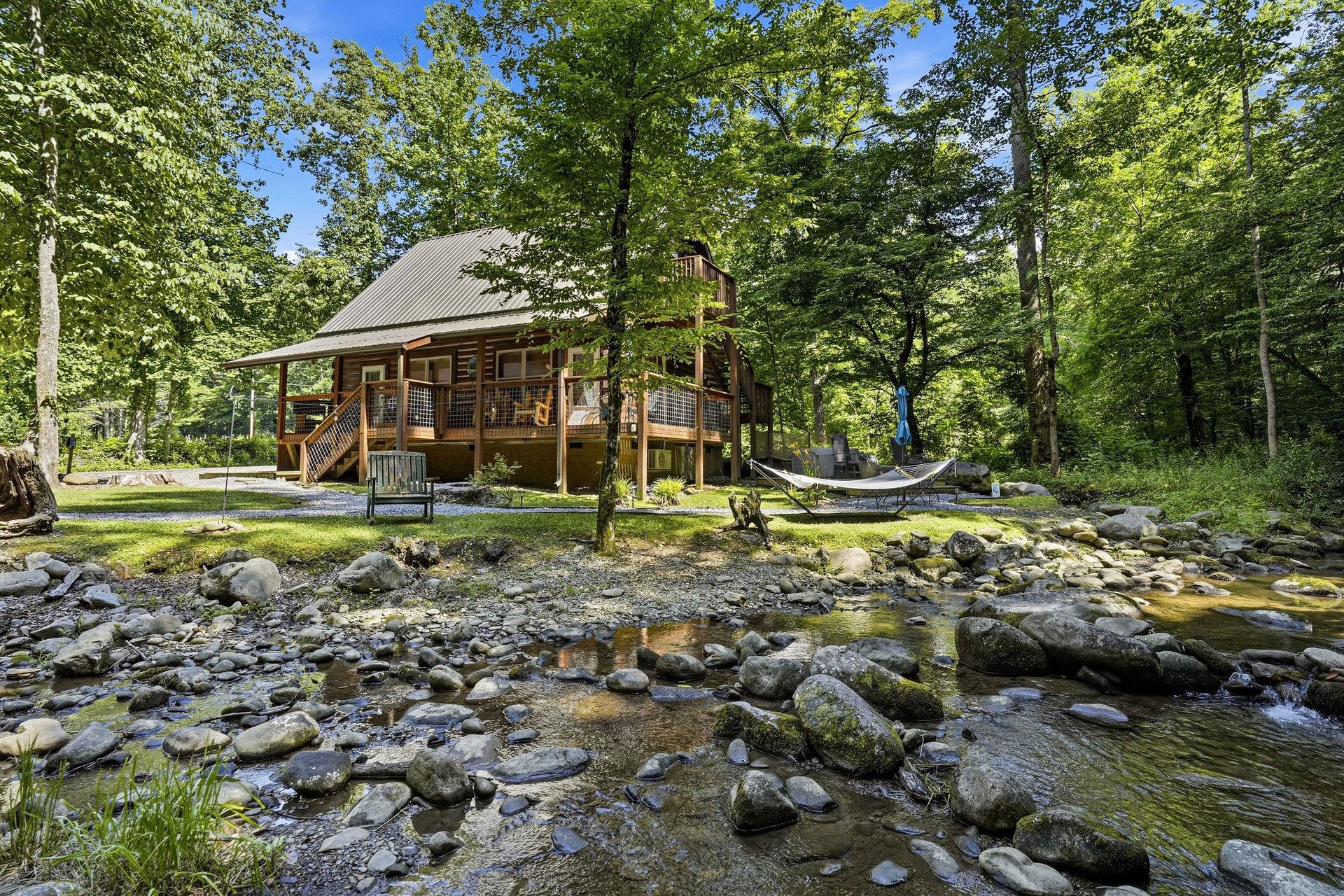 A rustic cabin nestled along a peaceful stream, surrounded by lush forest—the perfect setting for your private mountain escape, complete with hammock and plenty of outdoor space to unwind.