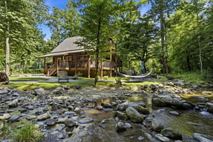 A rustic cabin nestled along a peaceful stream, surrounded by lush forest—the perfect setting for your private mountain escape, complete with hammock and plenty of outdoor space to unwind.