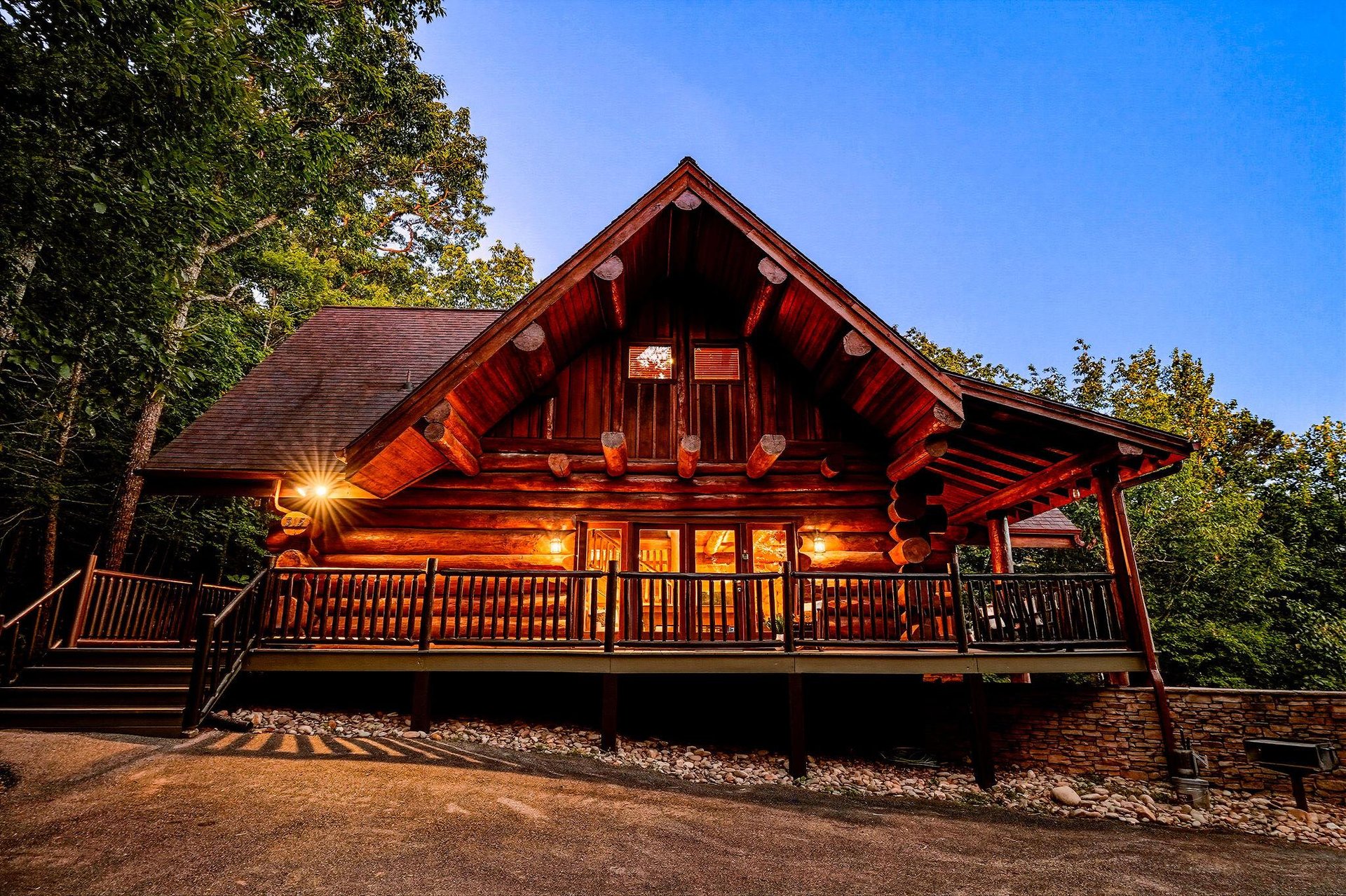 A handsome log cabin surrounded by trees offers rustic charm and warmth as dusk settles in, making for an inviting woodland retreat.